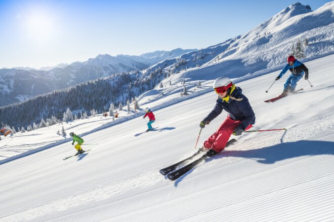 Die Freude am Skifahren in Flachau. Am Bild sieht man eine Gruppe von 4 Skifahrern auf der Piste. Im Hintergrund erkennt man den Starjet 3 und die Bergwelt in Flachauwinkl.