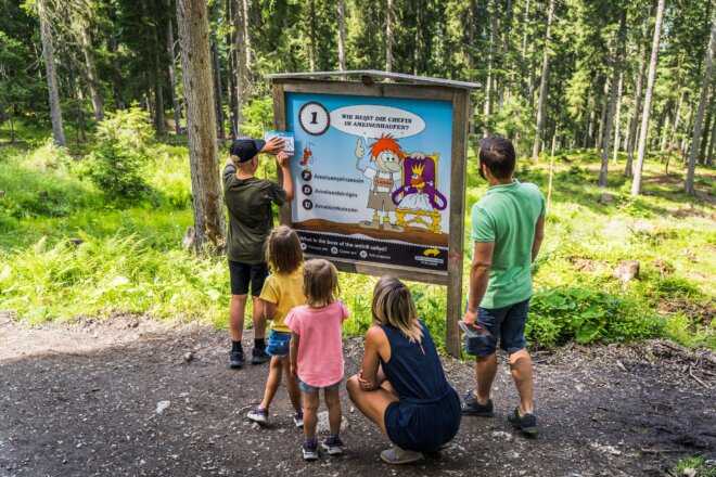 Der Flori's Erlebnispfad ist das Wander-Highlight für Kids in Flachau. Am Bild zu sehen ist eine Familie mit 3 Kids vor einer Rätselstation von Flori's Erlebnispfad.