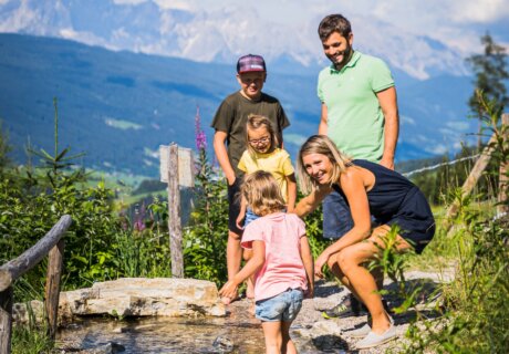 Der Flori's Erlebnispfad ist das Wander-Highlight für Kids in Flachau. Am Bild zu sehen ist eine Familie mit 3 Kids bei einer Wasser-Spiel-Station auf Flori's Erlebnispfad.