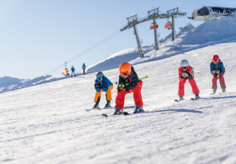 Pistenskifahren in Flachau. Am Bild sieht man: eine Familie die in der Hocke hinunterfährt. Im Hintergrund erkennt man die Skistation Starjet 3.