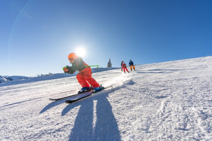 Pistenskifahren in Flachau. Am Bild sieht man: eine Familile mit 4 Personen, in Hocke die herrliche Piste in Flachau bei sonnigem Wetter hinunterfahren.