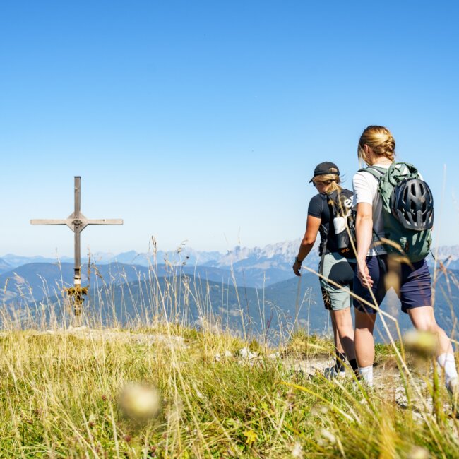 Wanderung auf den Lackenkogel in Flachau. Am Bild sieht man zwei Mädels auf das Gipfelkreuz des Lackenkogels zugehen.