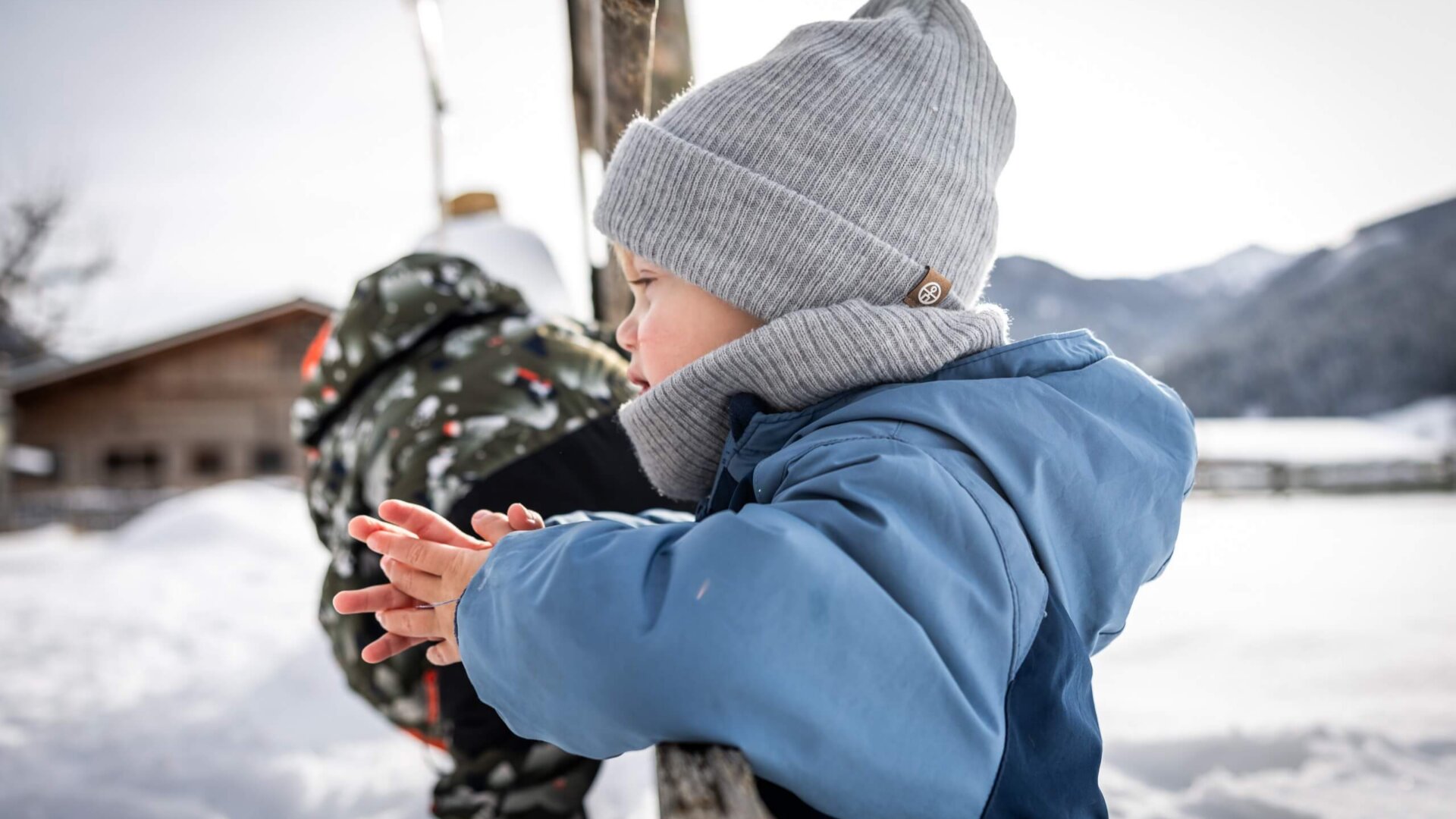 Kind lehnt im Schnee am Zaun