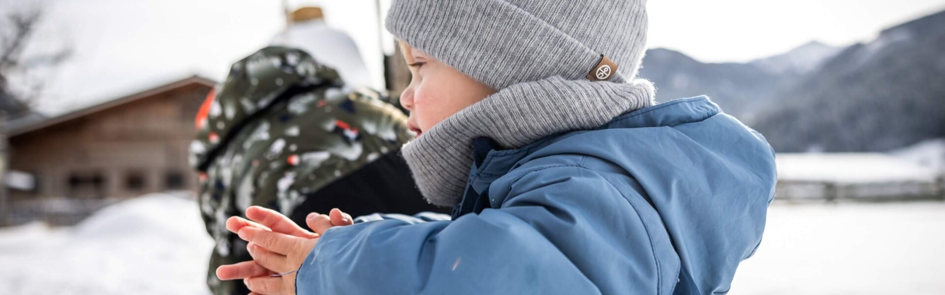 Kind lehnt im Schnee am Zaun