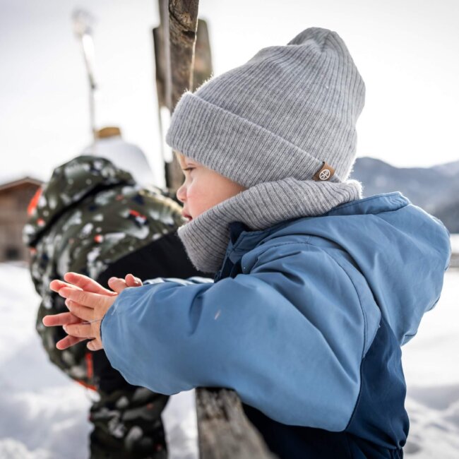 Kind lehnt im Schnee am Zaun