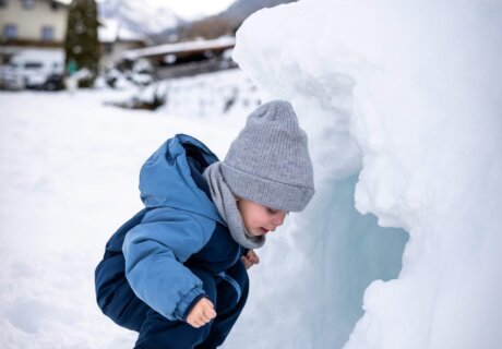 Kleines Kind schaut in eine Schneehöhle im Schnee