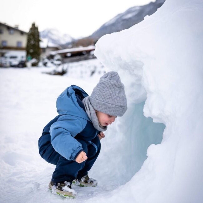 Kleines Kind schaut in eine Schneehöhle im Schnee