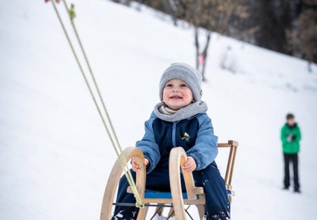 Kleines Kind sitzt auf Holzschlitten und wird im Schnee gezogen