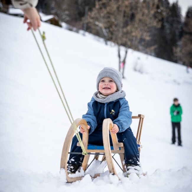 Kleines Kind sitzt auf Holzschlitten und wird im Schnee gezogen