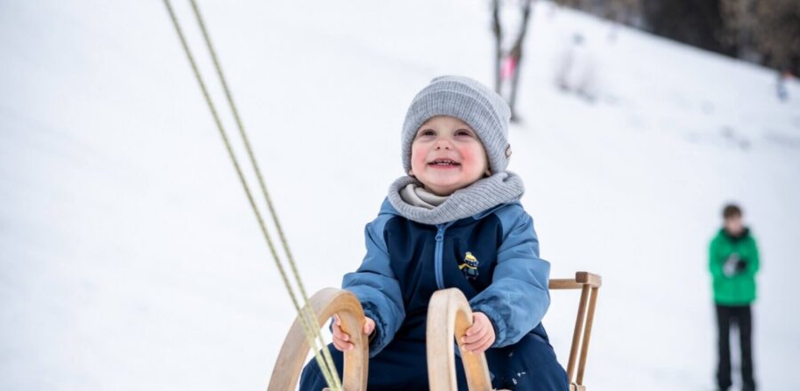 Kleines Kind sitzt auf Holzschlitten und wird im Schnee gezogen