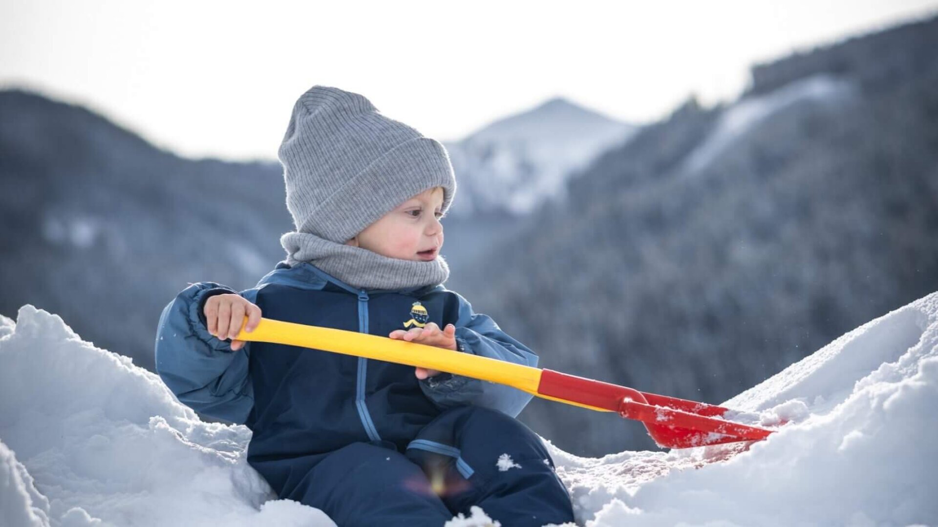 Kleines Kind spielt mit Schaufel im Schnee in den Bergen