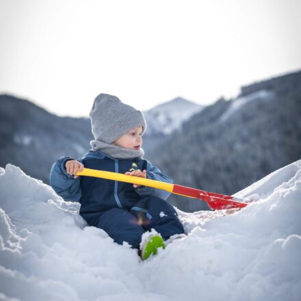 Kleines Kind spielt mit Schaufel im Schnee in den Bergen