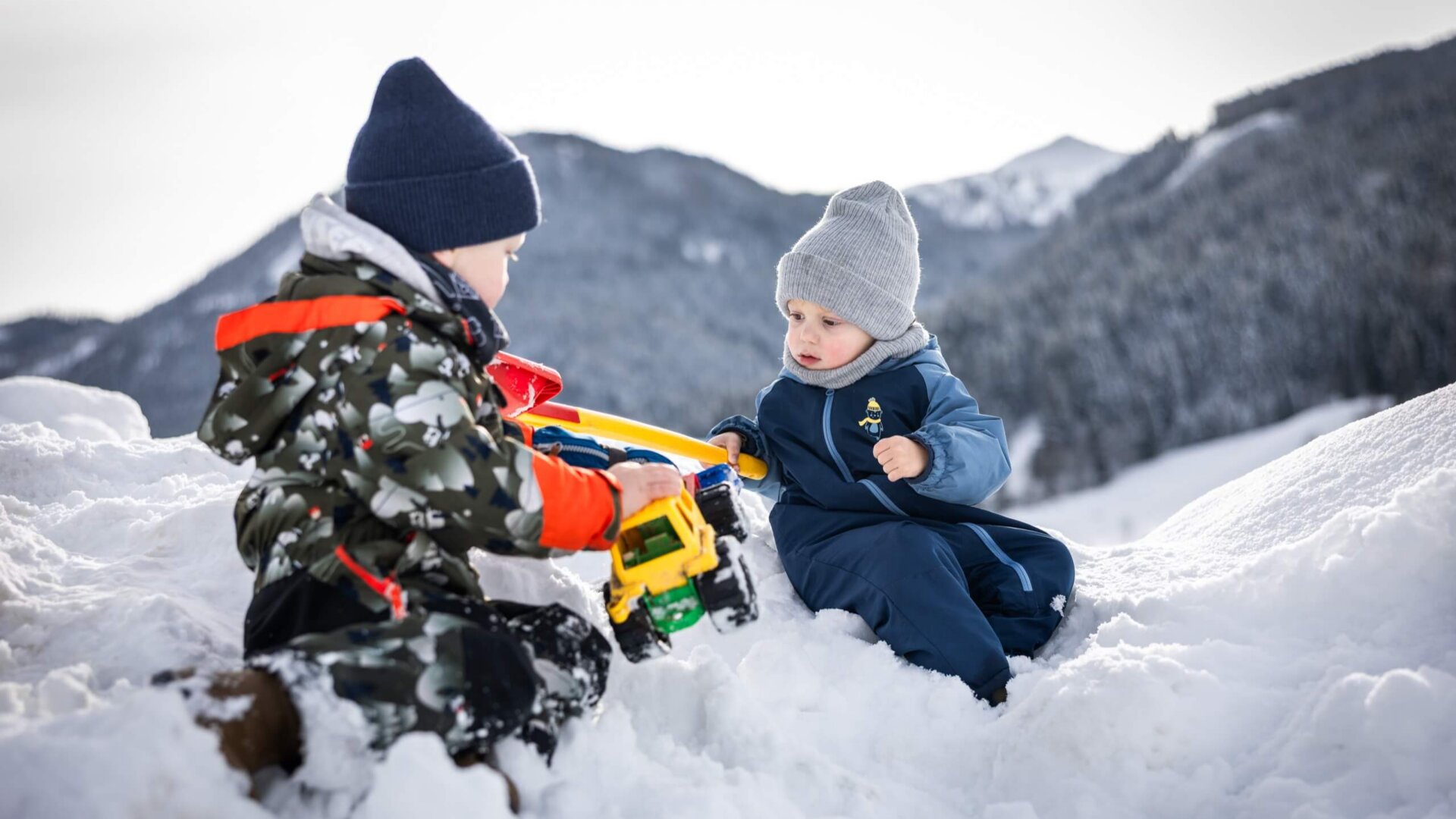 Zwei Kinder spielen mit Traktor im Schnee