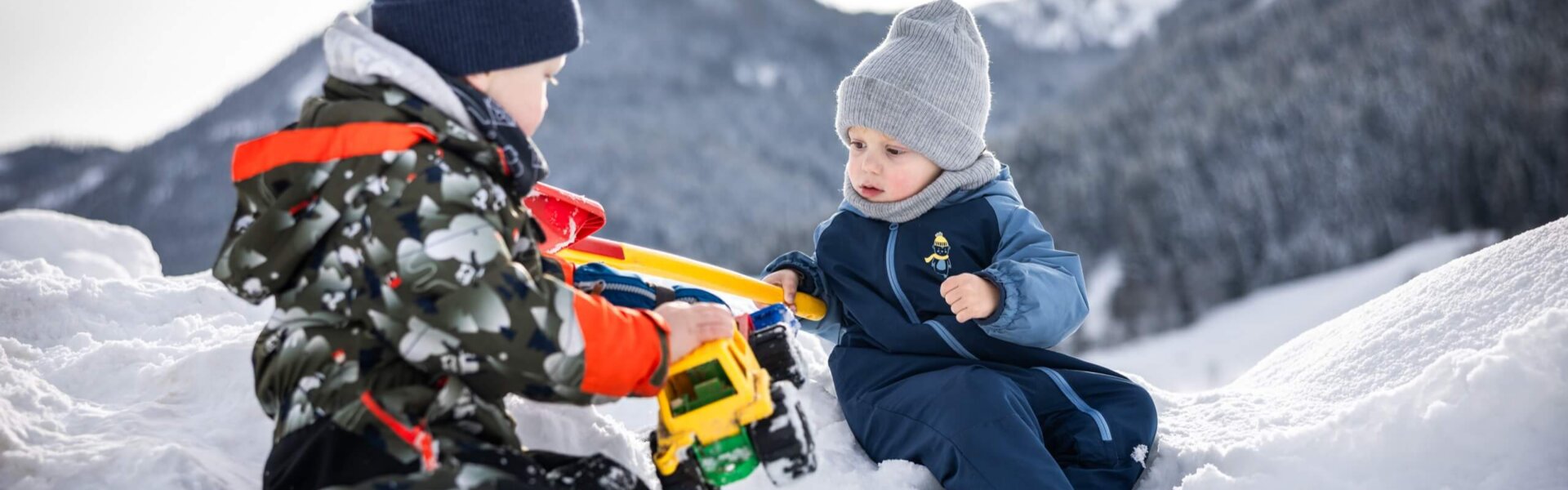Zwei Kinder spielen mit Traktor im Schnee