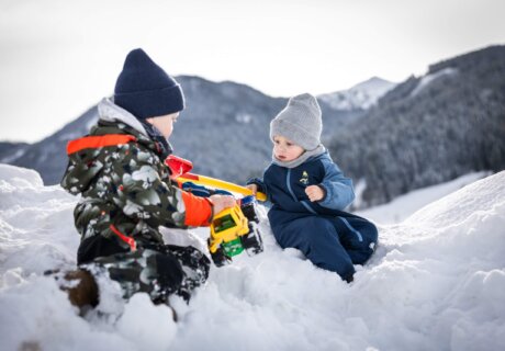 Zwei Kinder spielen mit Traktor im Schnee