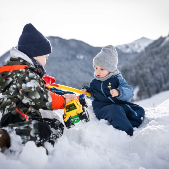 Zwei Kinder spielen mit Traktor im Schnee