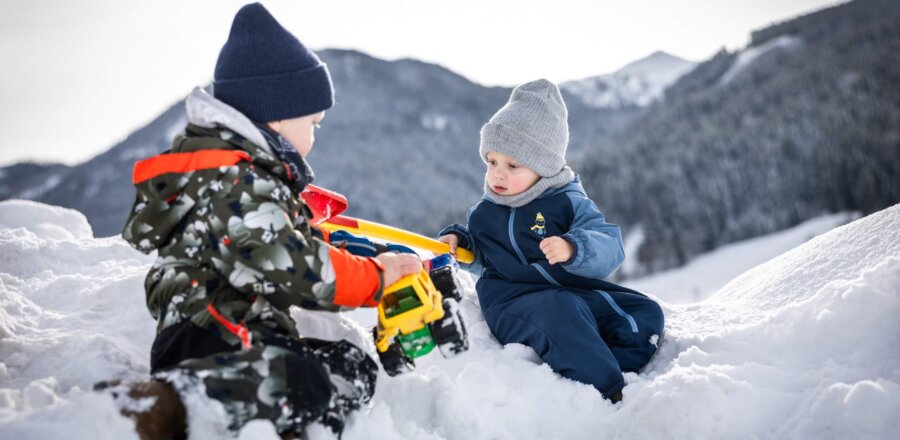 Zwei Kinder spielen mit Traktor im Schnee