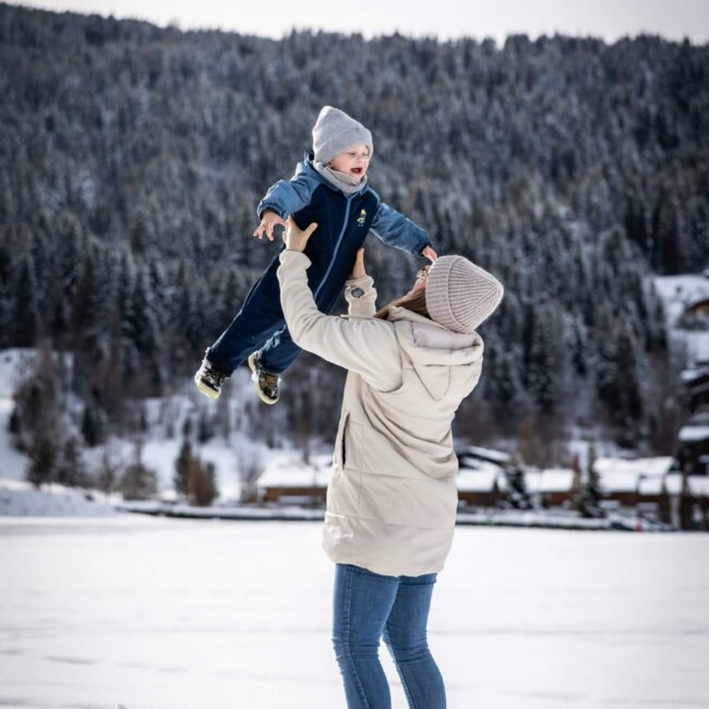 Mutter spielt mit Kind im Schnee und wirft es lachend in die Luft